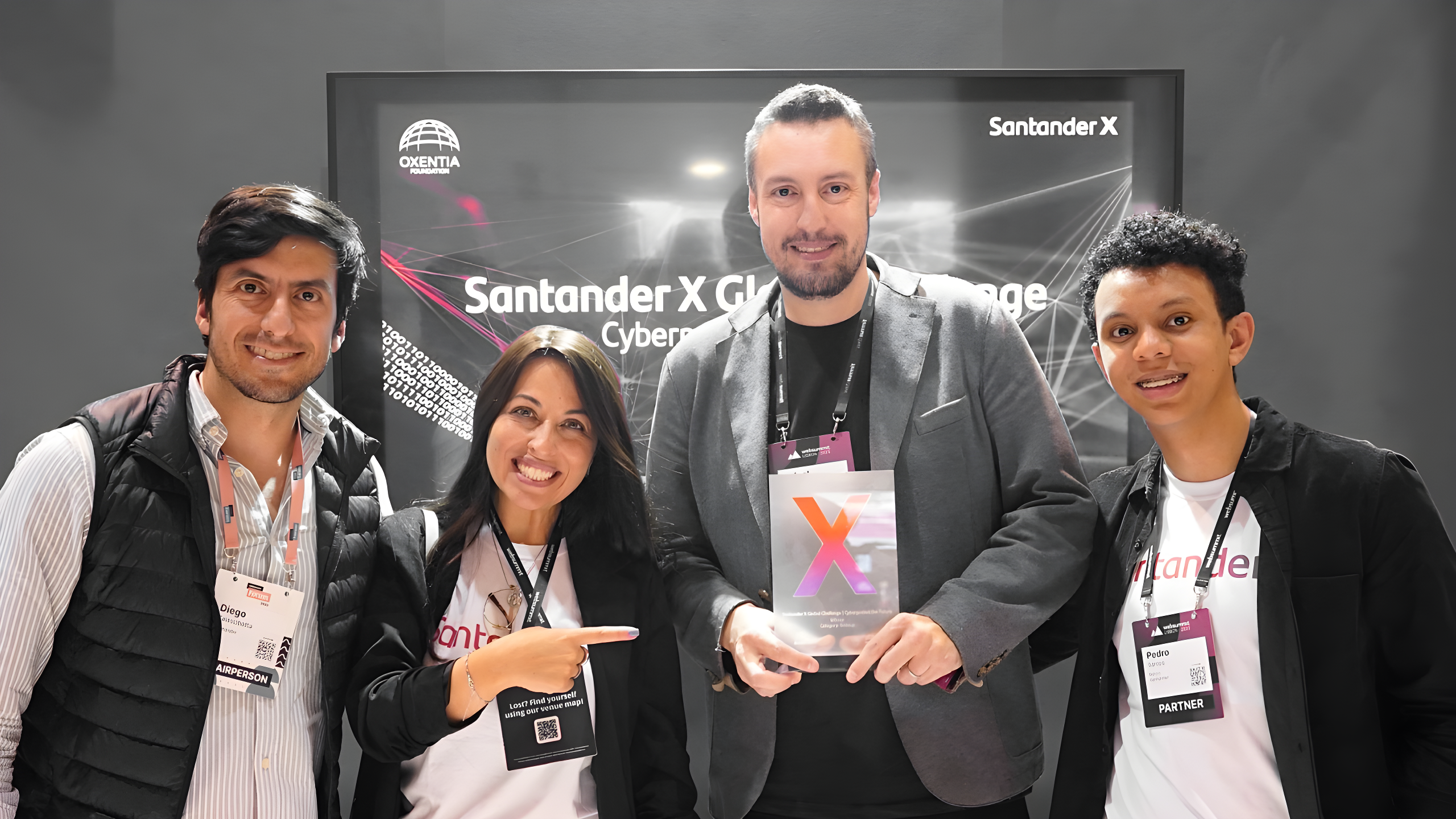La imagen muestra a un grupo de personas posando para una foto durante la ceremonia de premiación del Santander X Global Challenge. Hay cuatro individuos sonriendo. Rafael Umann, el CEO de Azion, está en el centro, sosteniendo el premio.