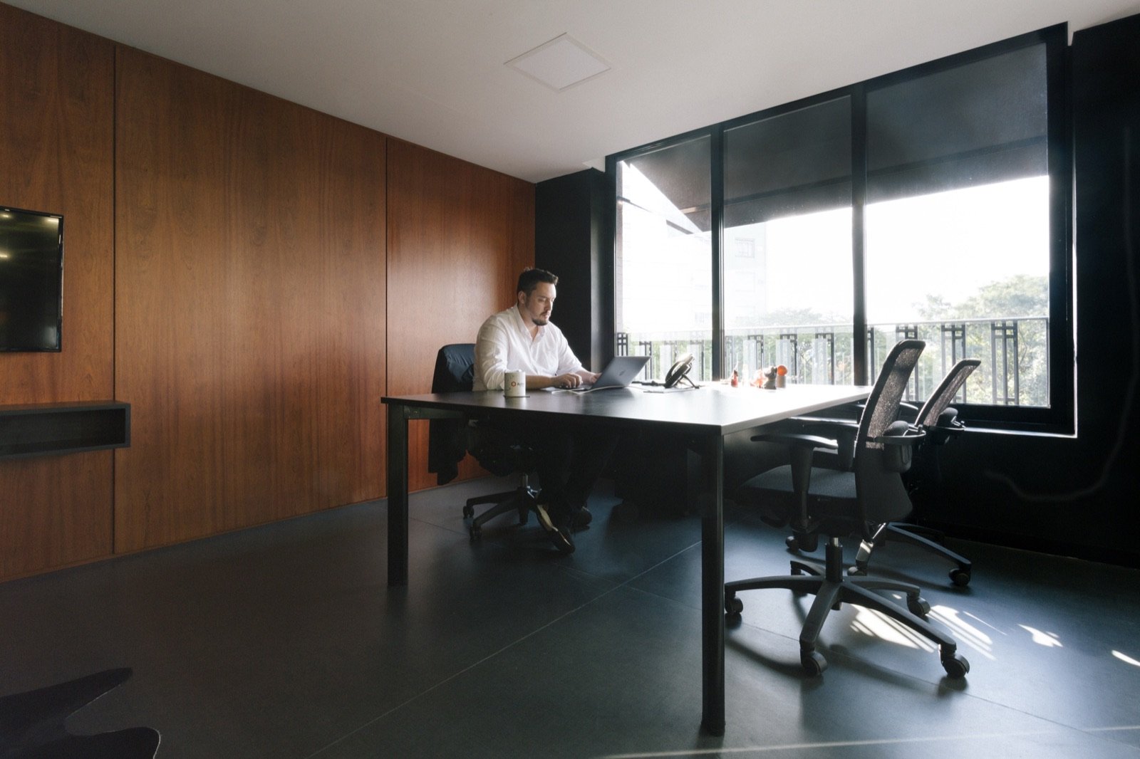 Sala de reunião com painéis de madeira e uma pessoa trabalhando no notebook perto da janela