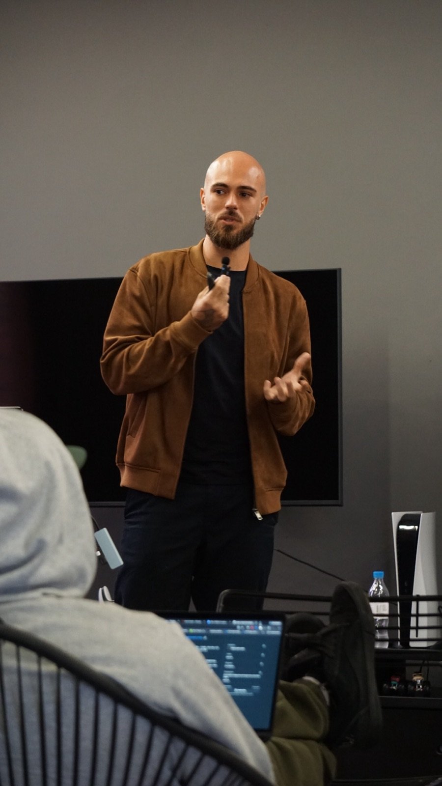 Integrante do time apresentando em frente a uma tela enquanto colegas assistem com notebooks